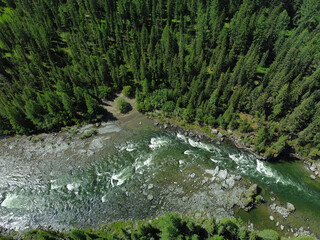 Aerial view of a green mountain landscape and alpine meadows where a river flows from the mountains and a beautiful coniferous forest stretches.
