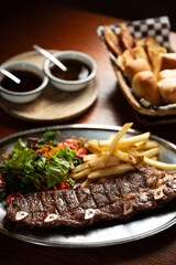Strip roast with french fries and salad on wooden table with glass of red wine. Argentine restaurant concept. Gastronomy concept