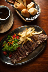 Strip roast with french fries and salad on wooden table with glass of red wine. Argentine...
