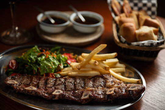 Strip roast with french fries and salad on wooden table with glass of red wine. Argentine restaurant concept. Gastronomy concept