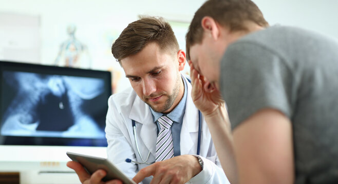 Portrait of serious doctor indicating bad diagnosis to sad and unsettling patient. Man explaining to visitor treatment method. Medicine and healthcare concept. Blurred background