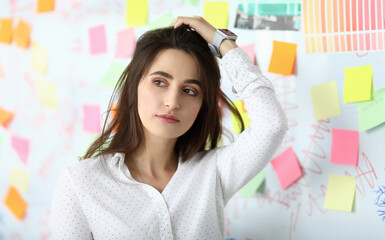 Portrait of pretty businesswoman standing near white board with empty colorful sticker and touching...