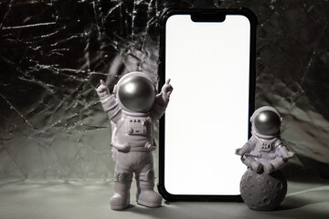Plastic toy figure astronaut with mobile phone white screen for your advertisement Copy space. Concept of out of earth travel, private spaceman commercial flights. Space missions and Sustainability