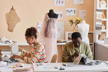Two young creative African American designers or stylists sewing new clothes while customizing old...