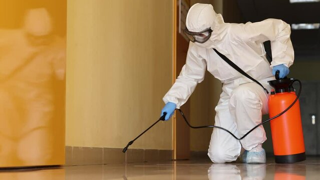 Employee in a protective suit wearing protective mask disinfects room. Disinfection from bacteria virus and insects concept