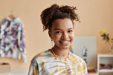 Fototapeta premium Happy young woman in tie dye t-shirt standing in front of camera in workshop, craft studio or atelier creating new stylish and trendy attire