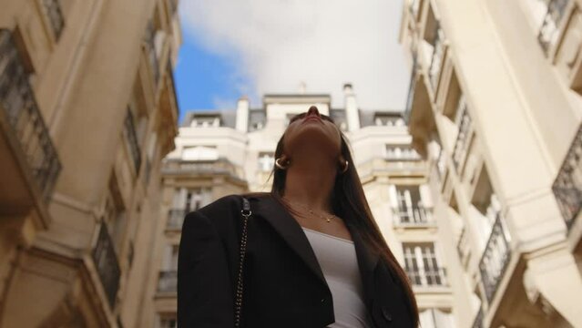Female tourist with brown hair looking up at buildings while walking in Paris