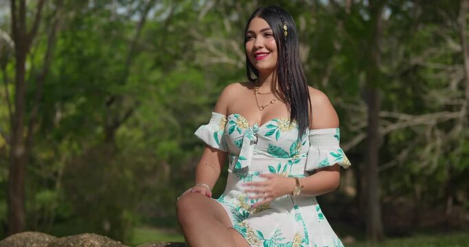Hispanic girl sits on a tree trunk in the park in a sexy short dress
