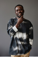 Young stylish African American man in trendy pullover touching his face while posing in studio over grey background during photo session