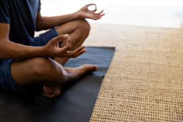 Midsection of biracial man doing yoga and meditating at home, copy space