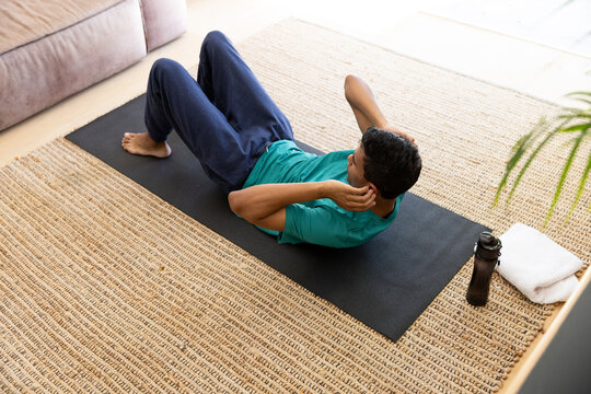 Biracial Man Exercising And Doing Sit Ups On Mat At Home