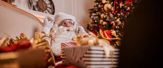 Santa Claus talking on phone sitting neat christmas tree with gifts. New year and Merry Christmas 
