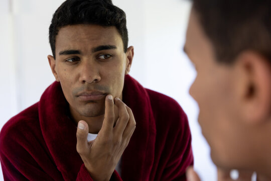 Biracial Man Touching His Face Looking In Mirror In Bathroom At Home