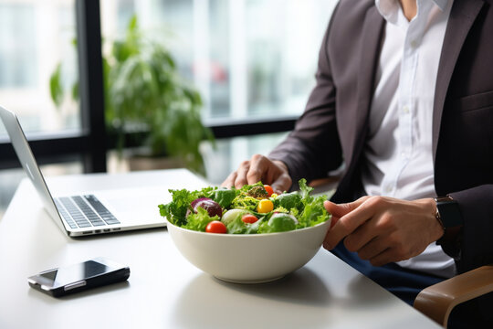 Man in suit unrecognizable torso eating healthy business lunch in modern office interior, Businessman at working place with vegetable salad in bowl, diet and right nutrition concept