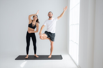 Fototapeta premium Young couple practicing yoga in a white room of studio.