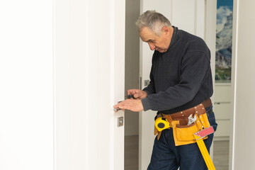 Mature man himself installs the door hinges with a screwdriver