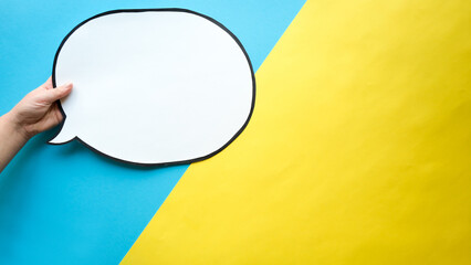 Speech bubble in a hands on a blue and yellow background. Comic cloud with a place for text