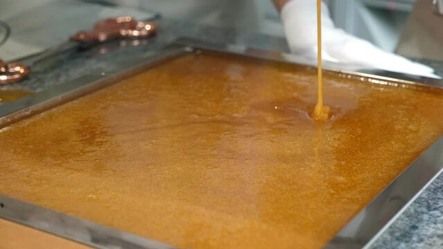A woman works in a pastry shop and prepares caramel, she pours liquid caramel on the table. Working process in the confectionery industry. Stirring hot thick liquid caramel before making candies.