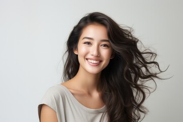 Naklejka premium Portrait of a smiling young Asian woman with flowing hair on a light background.