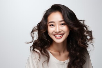 Portrait of a smiling young Asian woman with flowing hair on a light background.