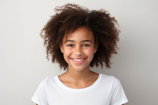 Portrait of a cheerful young girl with curly hair smiling on a light background.