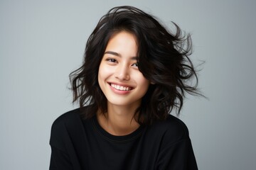 Fototapeta premium Portrait of a smiling young Asian woman with flowing hair on a light background.