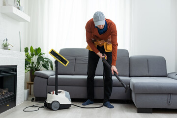 Dry cleaner's man employee removing dirt from furniture in flat, closeup, vacuum clean sofa with...