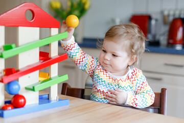 Little baby girl playing with educational toys at home or nursery. Happy healthy toddler child...