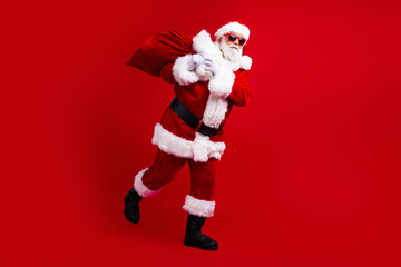 Photo of jolly funky man santa claus hat hand hold heavy bag deliver gifts north pole christmas magic isolated on red color background