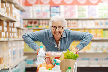 Cheerful funny senior woman pushing a full shopping cart