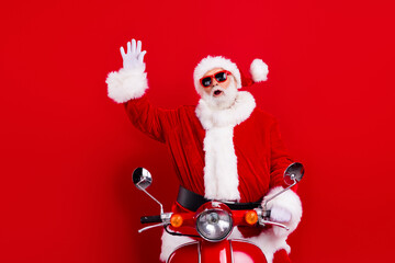 Portrait of cheerful santa claus with white beard in stylish sunglass driving scooter waving hand...