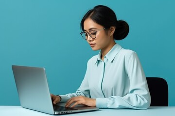 Asian Office Worker Focused On Laptop Against Blue Background