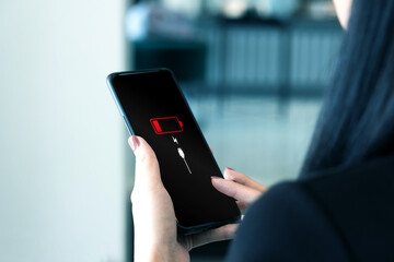 Close-up view of woman holding smartphone with low battery symbol notification on the screen....