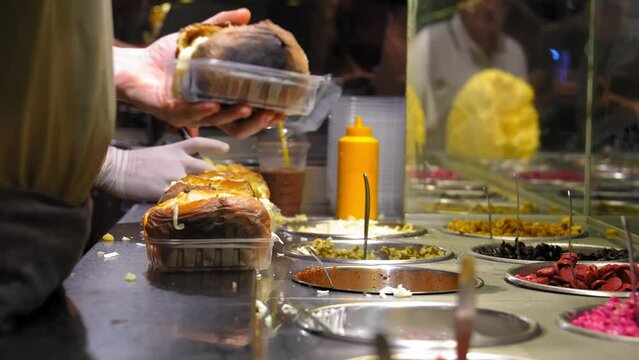 Chef prepares in Kumpir restaurant - traditional Turkish dish with baked potatoes, butter, cheese and vegetables. Turkish street food Kumpir. Baked potatoes with cheddar cheese, corn, sausage, ketchup