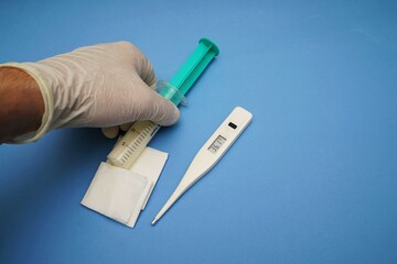 Hand with digital clinical thermometer and syringe on blue background