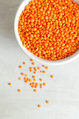 Orange lentils in a white bowl on a light background. The concept of proper nutrition. Vegan and vegetarian food. Vertical orientation. Top view. Copy space.