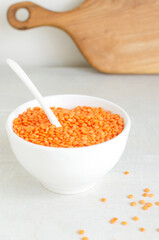 Fototapeta na wymiar Orange lentils in a white bowl with a teaspoon on a light background. The concept of proper nutrition. Vegan and vegetarian food. Vertical orientation.