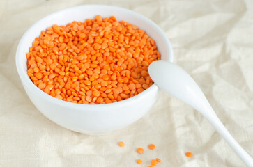 Orange lentils in a white bowl with a teaspoon on a linen tablecloth. The concept of proper...