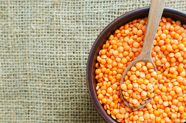Orange lentils in a brown ceramic bowl with teaspoon on a cutting board on a wooden table. Vegan and vegetarian food. Rustic style. Horizontal orientation. Top view. Copy space