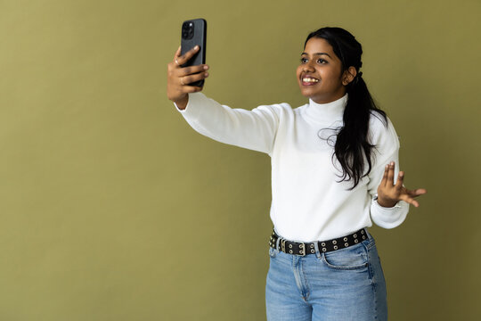 Indian woman over green background smiling and taking a selfie ready to post it on her social media.