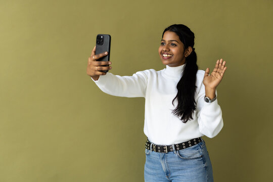 Indian woman over green background smiling and taking a selfie ready to post it on her social media.