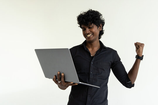 Happy excited indian man holding laptop standing isolated on gray background celebrating win, good online results
