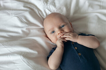 Baby boy teething, 3 months old, laying down on white sheets