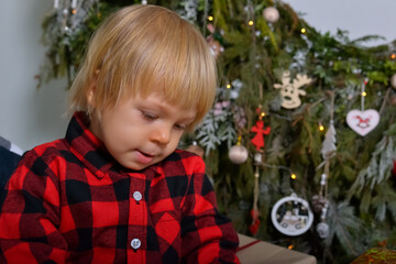 The happy kid is having fun with Christmas presents sitting on the background of the Christmas tree decorated with New Year's garlands. Family Christmas concept