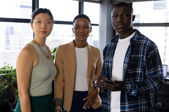 Portrait of three diverse male and female casual business colleagues standing in office, copy space