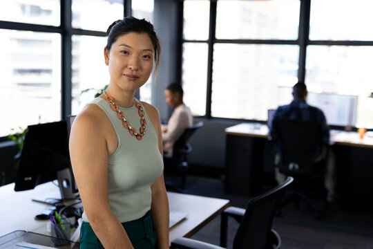 Portrait of happy asian casual businesswoman standing by desk in office, copy space