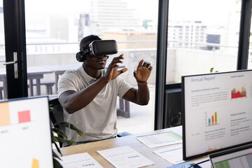 African american casual businessman wearing vr headset using virtual interface at office desk