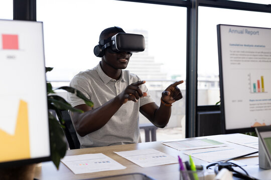 African american casual businessman wearing vr headset using virtual interface at office desk