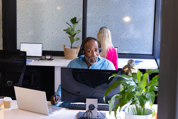Happy senior african american casual businessman in headphones having computer video call at office
