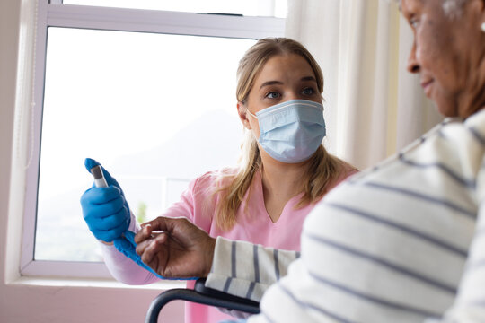 Caucasian female nurse in face mask using epi pen on senior african american woman